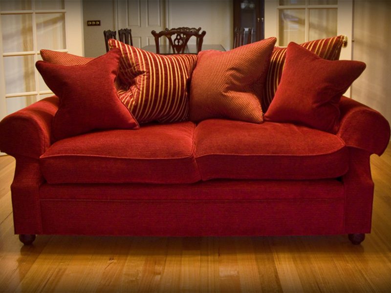 A deep red sofa piled with striped and plain cushions on a warm wooden floor